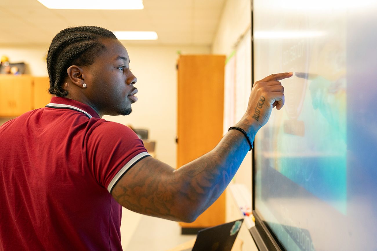 Teacher D’Marius Jones points at screen.