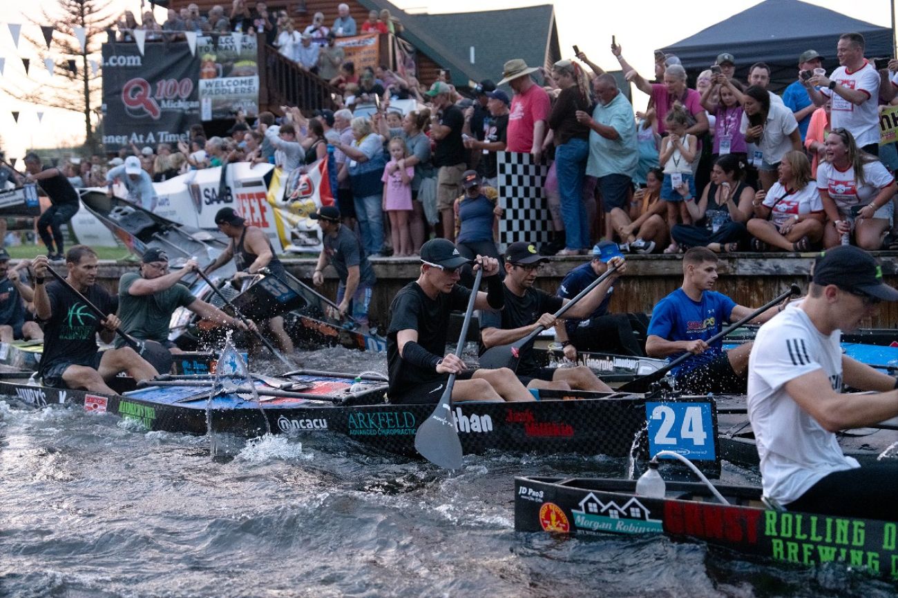 Canoe racers paddle down the Au Sable River while a crowd of spectators looks on