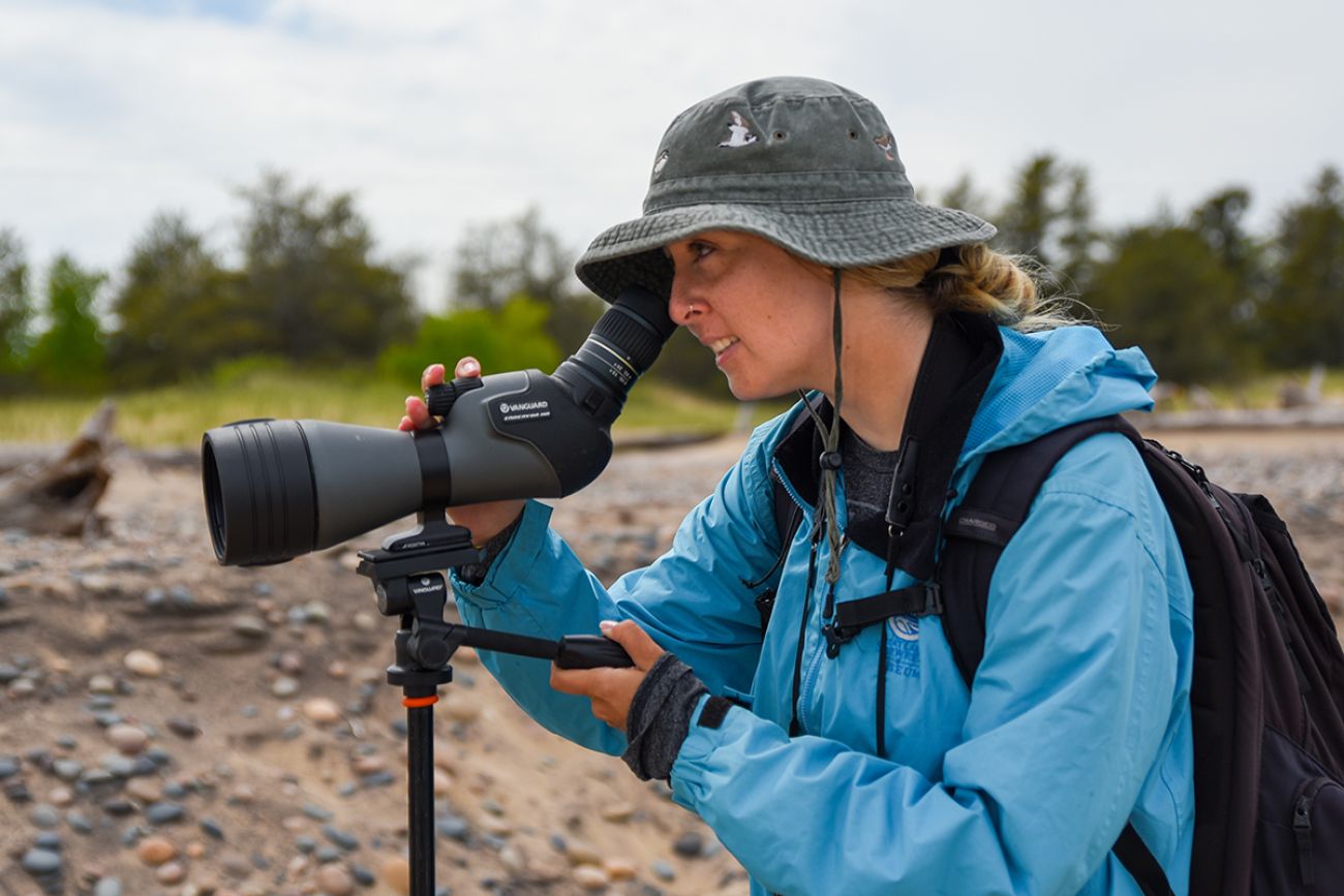 Stephanie Owens holds up a telescope on a beach.
