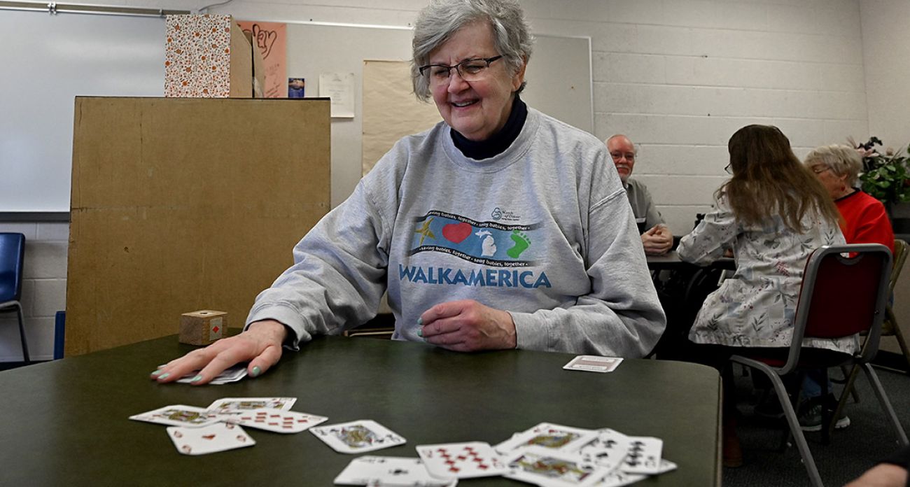 Mature, wearing a grey sweatshirt, woman deals cards