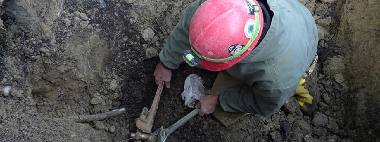 Plumber Ken Davison performing wrench work inside an excavated hole