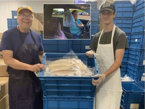 Workers pose with a crate of whitefish. Enbridge Energy and Massey Fish Company partnered to distribute free whitefish to area seniors, drawing cheers from allies and jeers from opponents who question the motives behind the company’s generosity. 