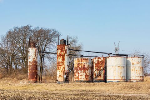 Old oil well storage tanks in farm field.