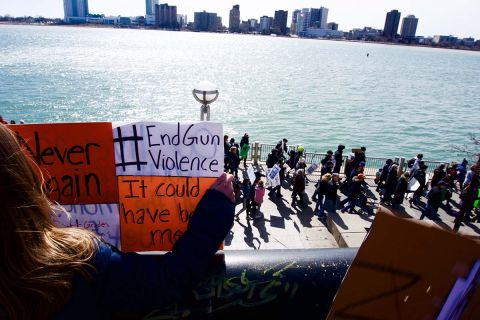 A girl holds a sign that says "#EndGunViolence" and "It could have been me" while looking down on protestors marching against gun violence