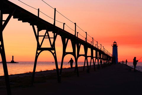 North Pier Lighthouse in Manistee Michigan on lake Michigan at sunset with fishermans silhouettes, in the late summer.
