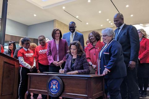 whitmer sitting at a desk with people surrounding her