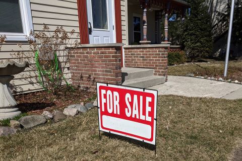 A red and white for sale sign in the front yard of a house