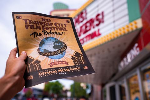 raverse City Film Festival on marquee at The State Theatre. Hand holding an official movie guide brochure for the event in front of theatre awning