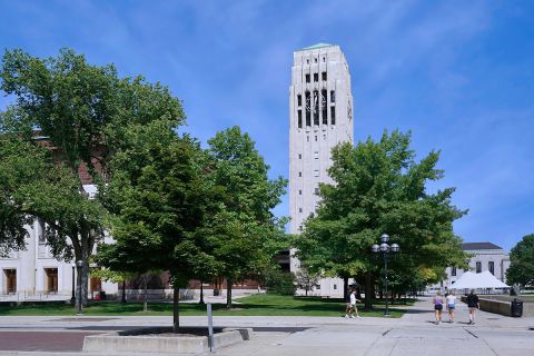 Students walk on the campus of the University of Michigan on a sunny day, with Burton Memorial Tower in the background.