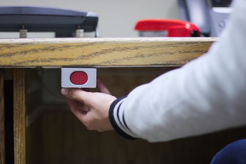 A hand ready to press a panic button under an administrative desk