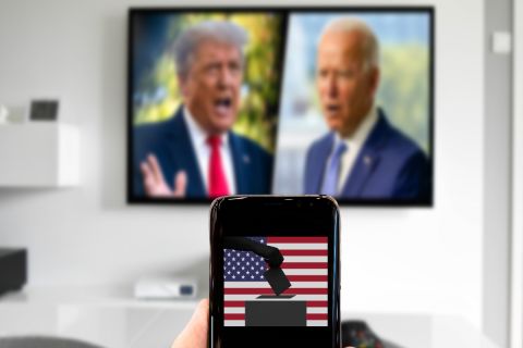 Person holds up phone with a voting box with a picture of Joe Biden and Donald Trump in the background