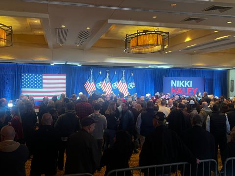 A crowd of people standing in a ballroom at the Detroit Marriott in Troy waiting for GOP presidential candidate Nikki Haley. Facing them are an American flag and Nikki Haley sign.