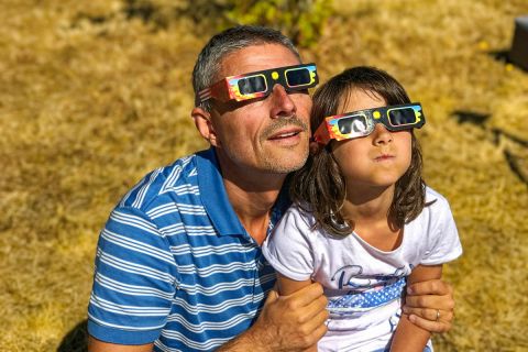 Father and daughter, family viewing solar eclipse with special glasses in a park.