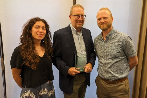 Three people stand in a line holding an award