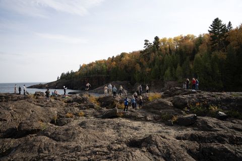 People standing, hanging out on dark-colored rocks at the Black Rocks at Presque Isle Park just north of downtown Marquette. 