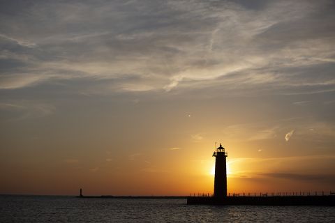 The sunset from Pere Marquette beach in Muskegon, Michigan. You can see a lighthouse.