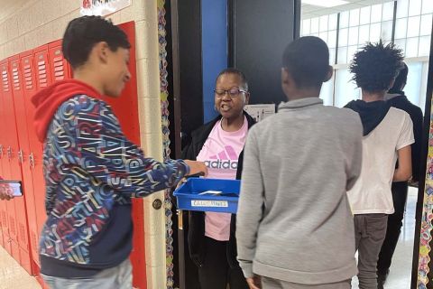 Kids put the cellphones in a container held by a teacher. 