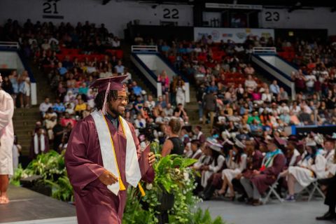 A young man in cap and gown picks up his high school diploma in an auditorium