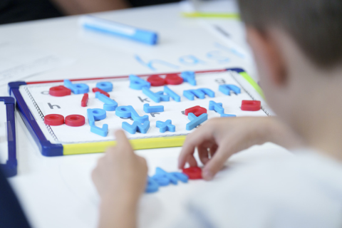 A view of a child from the back.  The student is participating in an activity that focuses on practicing letters. 