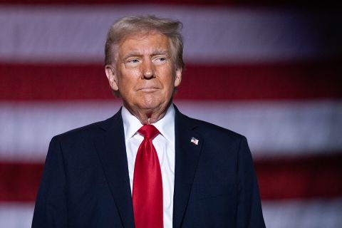 Donald Trump on a stage; American flag behind him. 