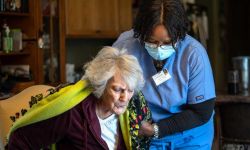 Excellacare Care Provider Sarah Sutherlin helps her client Carmela Palamara, 92, of Brownstown stand up to stretch her legs after the two color and play a game of UNO at Palamara's home on Wednesday, April 14, 2021. 