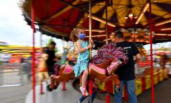 A young girl rides the merry-go-round while wearing a face mask