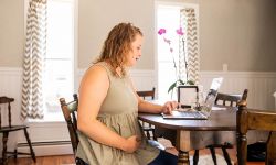 Abby Gilmore at a desk holding her stomach 