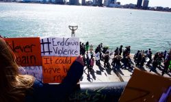 A girl holds a sign that says "#EndGunViolence" and "It could have been me" while looking down on protestors marching against gun violence