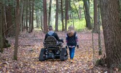 a person in an all-terrain wheelchair on a trail with a person walking beside them