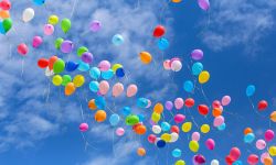 Multi-colored balls released into the blue sky.