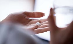 Close up woman holding pill in hand with water.