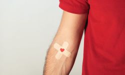 Partial view of patient in red t-shirt with plasters on grey background