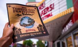 raverse City Film Festival on marquee at The State Theatre. Hand holding an official movie guide brochure for the event in front of theatre awning