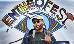 Kevin Boehnke speaking into a microphone. A banner that says "Entheofest" is behind him