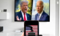Person holds up phone with a voting box with a picture of Joe Biden and Donald Trump in the background