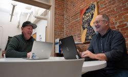 Two men laugh in an office on their computers