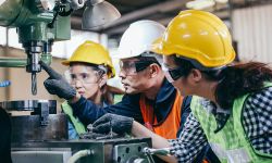 male foreman manager showing case study of factory machine to two engineer trainee