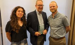 Three people stand in a line holding an award