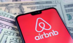 Airbnb app logo seen on the screen of smartphone, placed on dollar bills.