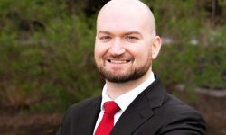 Ryan Hundt is wearing a black suit with a red tie