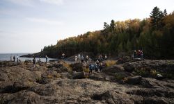 People standing, hanging out on dark-colored rocks at the Black Rocks at Presque Isle Park just north of downtown Marquette. 