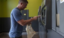 A man in a blue t-shirt places a plastic bottle into a bottle deposit machine.