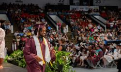 A young man in cap and gown picks up his high school diploma in an auditorium