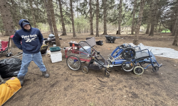 A man next to his personal items outside.