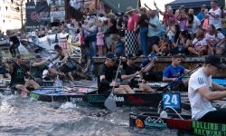Canoe racers paddle down the Au Sable River while a crowd of spectators looks on
