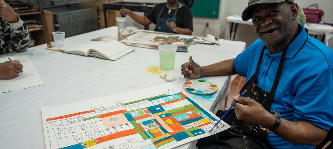 Ray Smith sits at a table while he paints. 