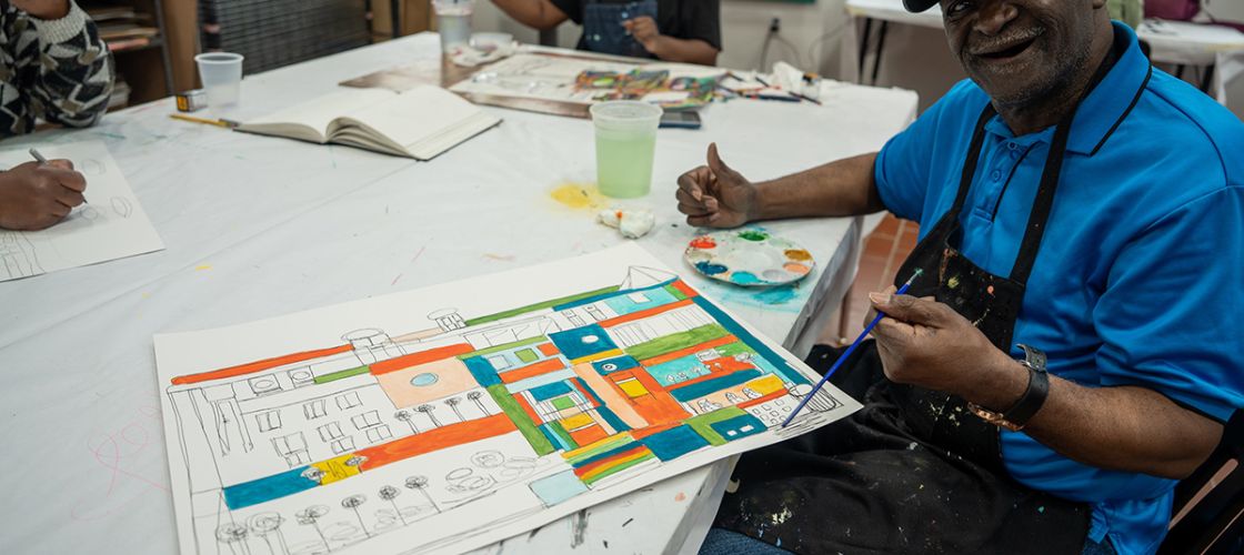 Ray Smith sits at a table while he paints. 
