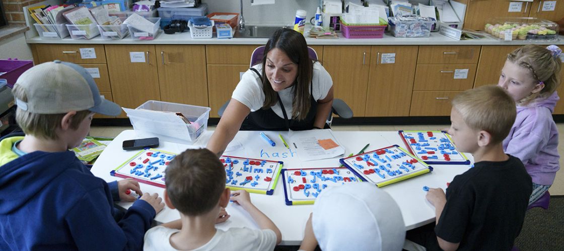 Becca Bradley sits at a table while interacting with students. 