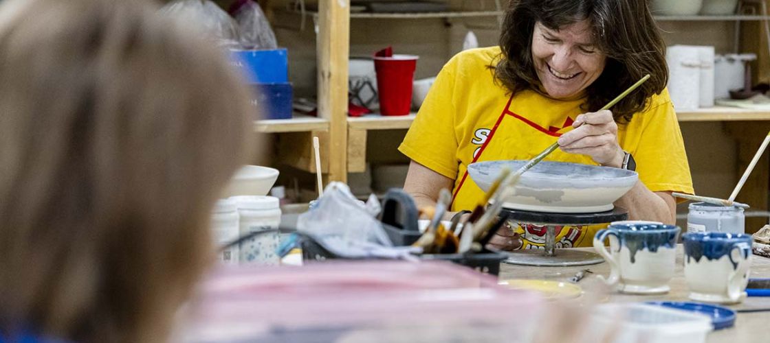 Margaret Afheldt smiles as she glazes a bowl. 