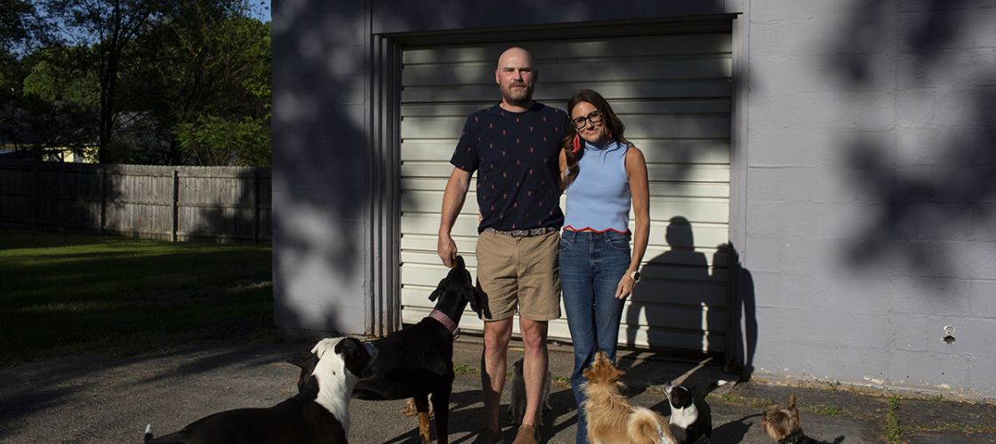 Kim Bode and Josh Byler pose outside. They are surrounded by dogs. 